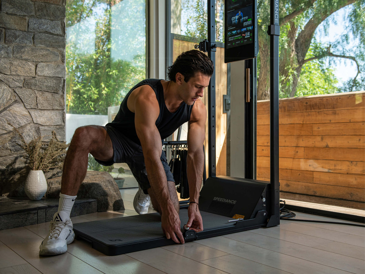 Ein Mann, der in einem häuslichen Umfeld auf einem Laufband trainiert. Im Hintergrund eine Steinwand und eine Glastür.